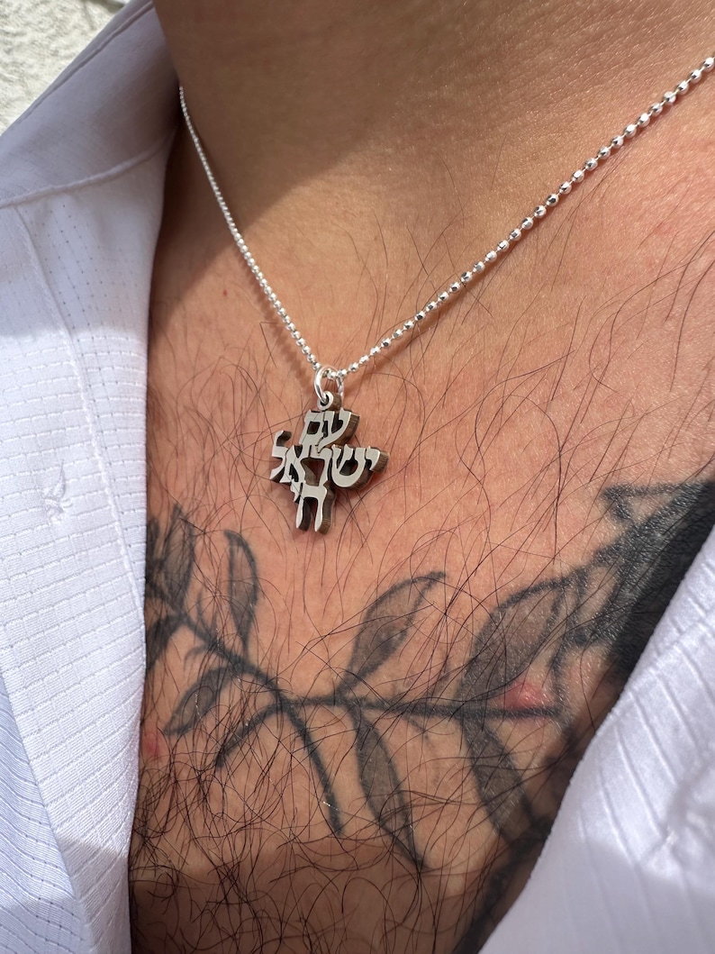 Puede incluir: Un collar de cadena de plata con un colgante con letras hebreas. El colgante tiene forma de &aacute;rbol con ramas y hojas.