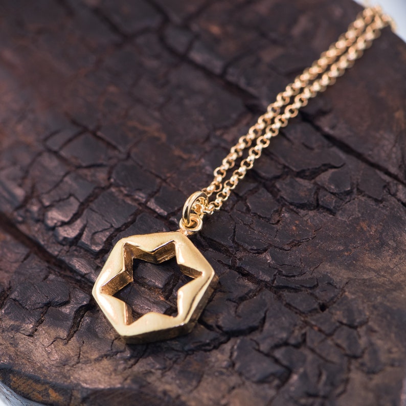 May include: A gold chain necklace with a star-shaped pendant. The pendant is a hollow hexagon with a five-pointed star cut out of the center.