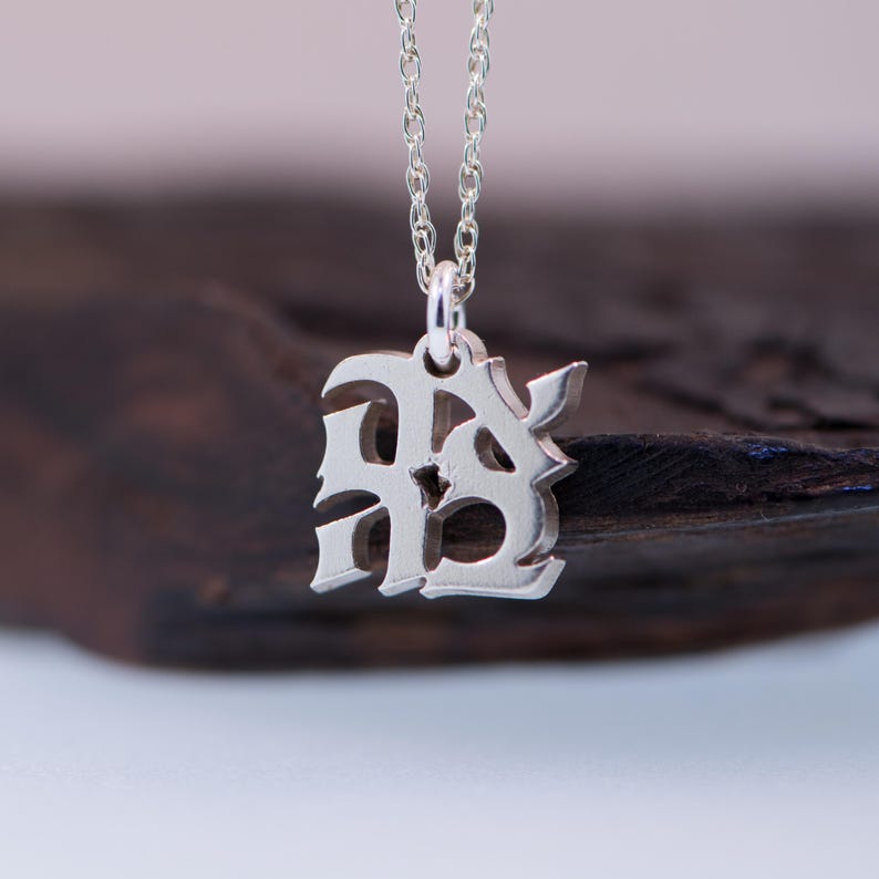 May include: A silver necklace with a pendant featuring the letters "RB" in a stylised, gothic font.