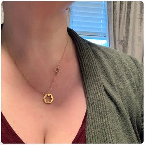 May include: A gold necklace with a star-shaped pendant and a small circle charm. The necklace is layered and has a delicate chain.