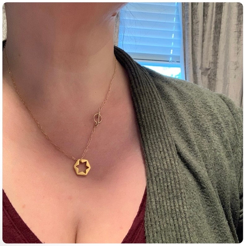 May include: A gold necklace with a star-shaped pendant and a small circle charm. The necklace is layered and has a delicate chain.