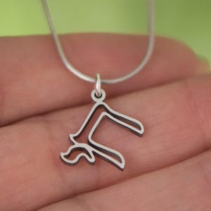 Peut inclure: Un collier avec un pendentif argent&eacute; repr&eacute;sentant un motif floral stylis&eacute;. Le pendentif est suspendu &agrave; une fine cha&icirc;ne argent&eacute;e. Le collier est pr&eacute;sent&eacute; sur un fond vert doux.
