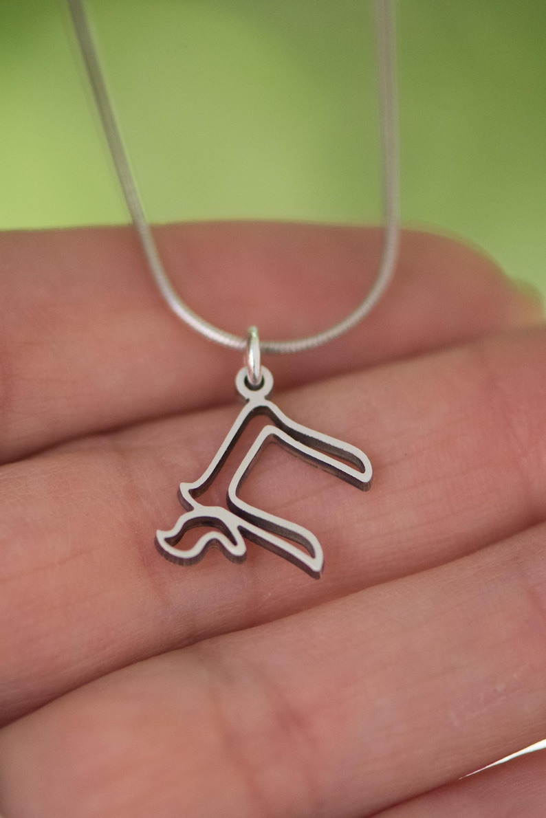 Peut inclure: Un collier avec un pendentif argent&eacute; repr&eacute;sentant un motif floral stylis&eacute;. Le pendentif est suspendu &agrave; une fine cha&icirc;ne argent&eacute;e. Le collier est pr&eacute;sent&eacute; sur un fond vert doux.