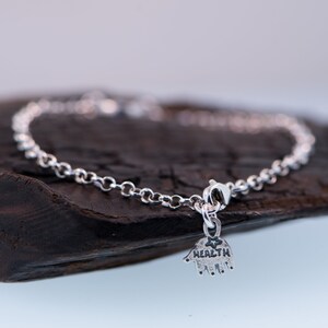 May include: A silver chain bracelet with a charm that says "HEALTH" and has a handprint design.
