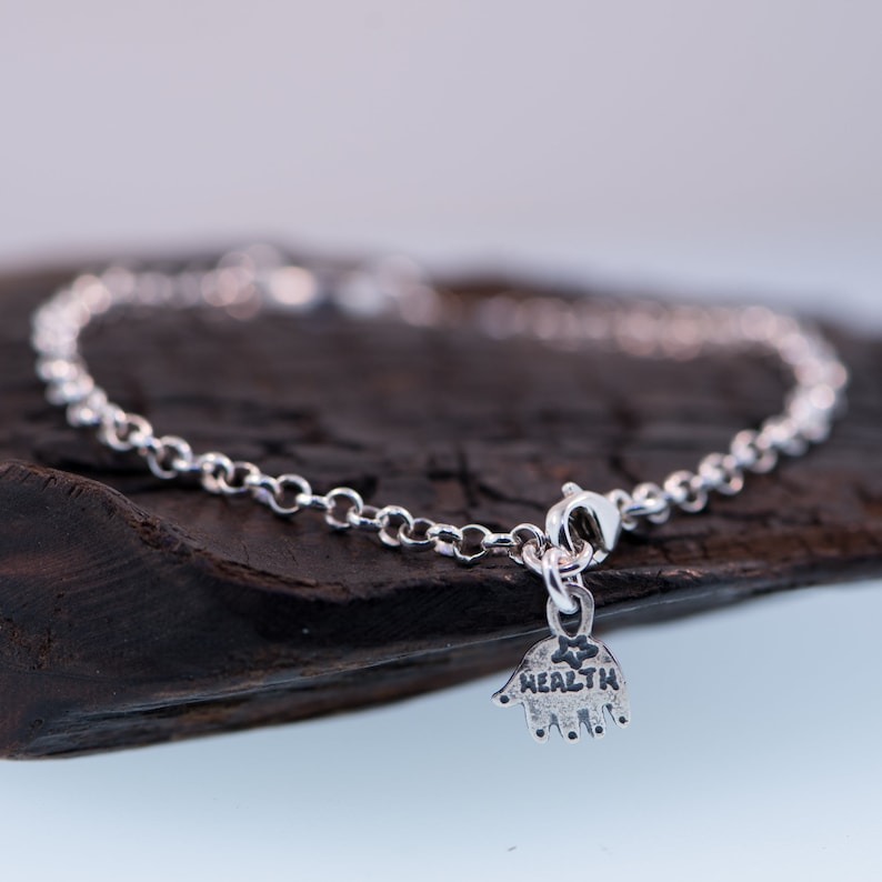 May include: A silver chain bracelet with a charm that says "HEALTH" and has a handprint design.