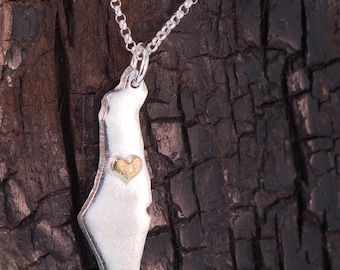 Op de afbeelding: Een zilveren ketting met een hanger in de vorm van de omtrek van Israël. De hanger heeft een klein gouden hart in het midden.