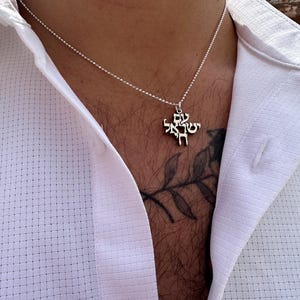 Puede incluir: Un collar de cadena de plata con un colgante con texto en hebreo. El colgante tiene forma de cruz.