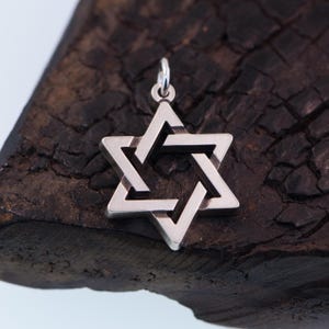May include: A silver Star of David pendant with a geometric design. The pendant is on a dark brown wooden surface.
