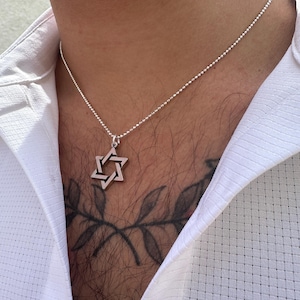 May include: A silver chain necklace with a silver Star of David pendant. The necklace is worn by a person with a tattoo of a branch on their chest.