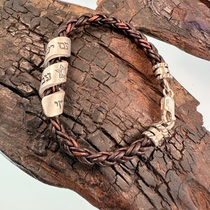 May include: A brown leather braided bracelet with silver charms. The charms have Hebrew lettering and a Star of David.