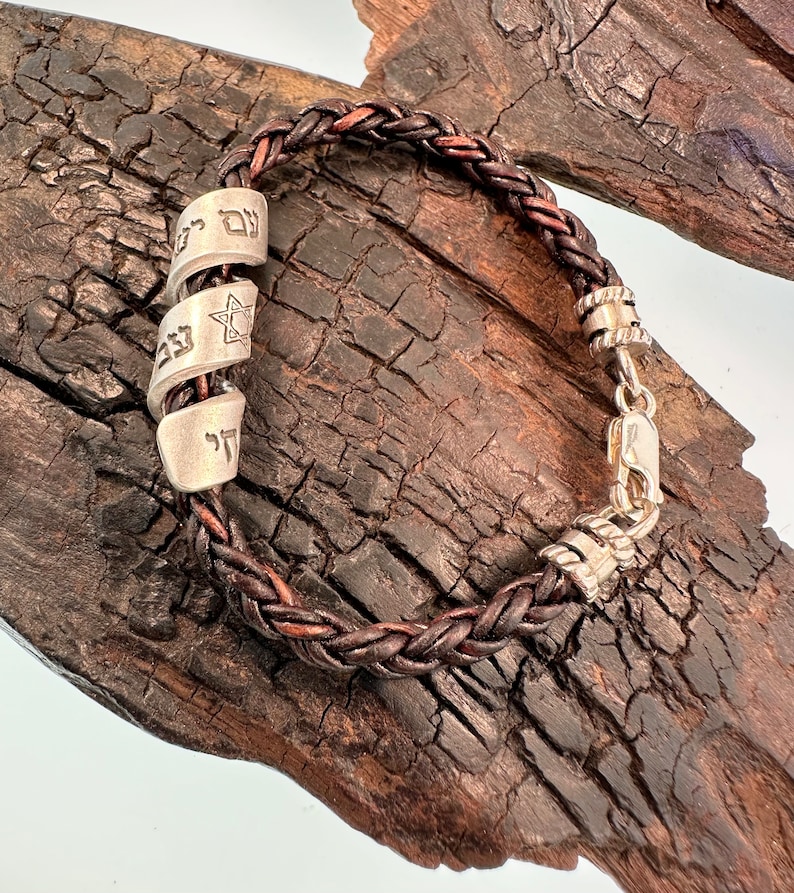 May include: A brown leather braided bracelet with silver charms. The charms have Hebrew lettering and a Star of David.