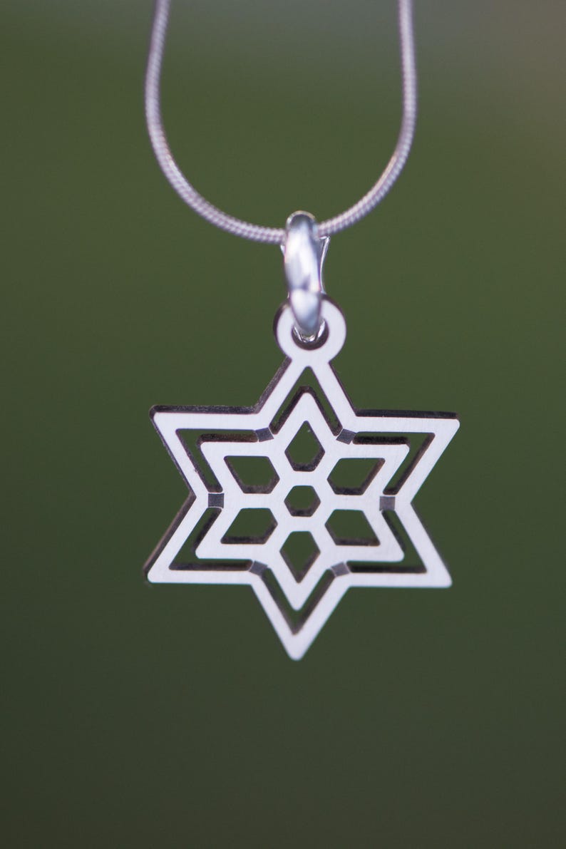 May include: A silver-colored pendant necklace featuring a Star of David design. The pendant is a six-pointed star with a detailed, openwork pattern. The necklace has a delicate chain and a simple clasp.