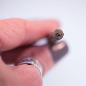 May include: Close-up of a metal stamp with the number .999 stamped on the end.