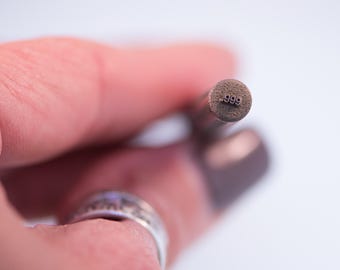May include: Close-up of a metal stamp with the number .999 stamped on the end.