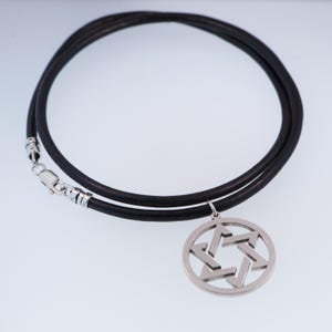 Pu&ograve; includere: Una collana in pelle nera con un ciondolo a forma di Stella di David color argento. Il ciondolo &egrave; una stella a sei punte all'interno di una cornice circolare. La collana ha una chiusura argentata.