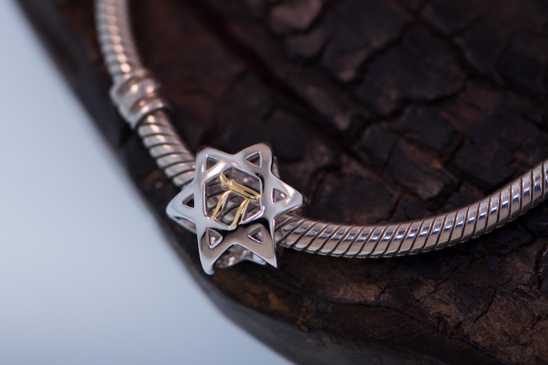 K&ouml;nnte beinhalten: Ein silbernes Armband mit einem silbernen und goldenen Davidstern-Anh&auml;nger. Der Anh&auml;nger ist mit einem hebr&auml;ischen Buchstaben in der Mitte verziert.