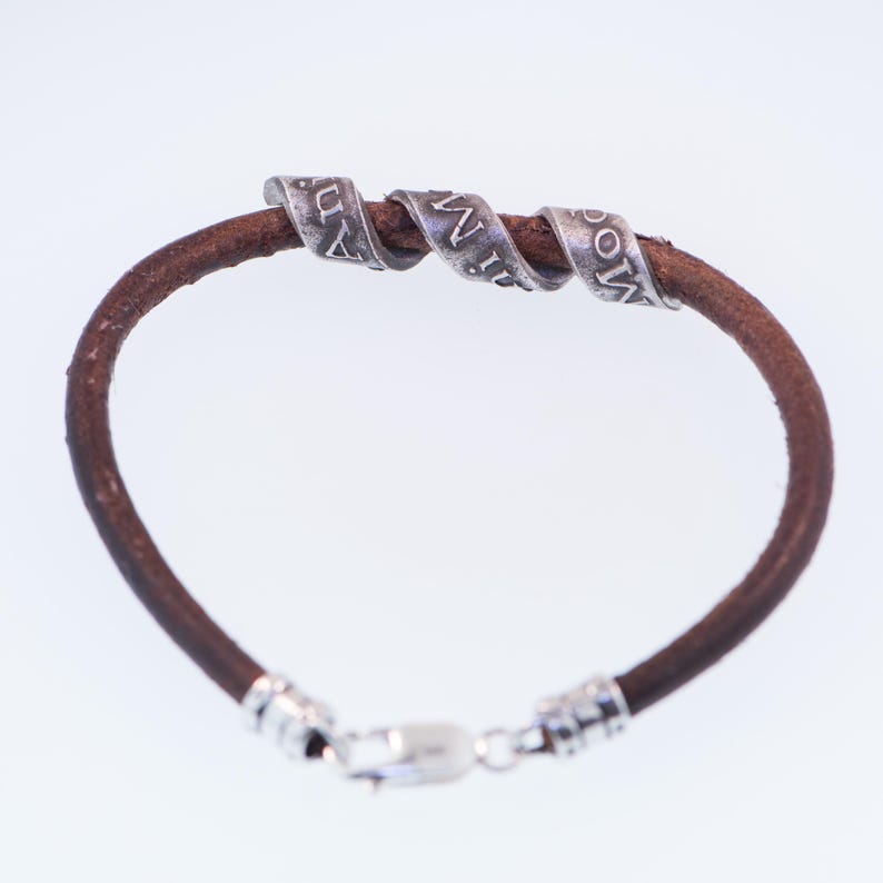 May include: A brown leather bracelet with three silver-coloured, spiralled bands. Each band has engraved text. The bracelet has a silver clasp.