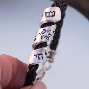 May include: A brown leather bracelet with silver charms featuring Hebrew text and a Star of David.