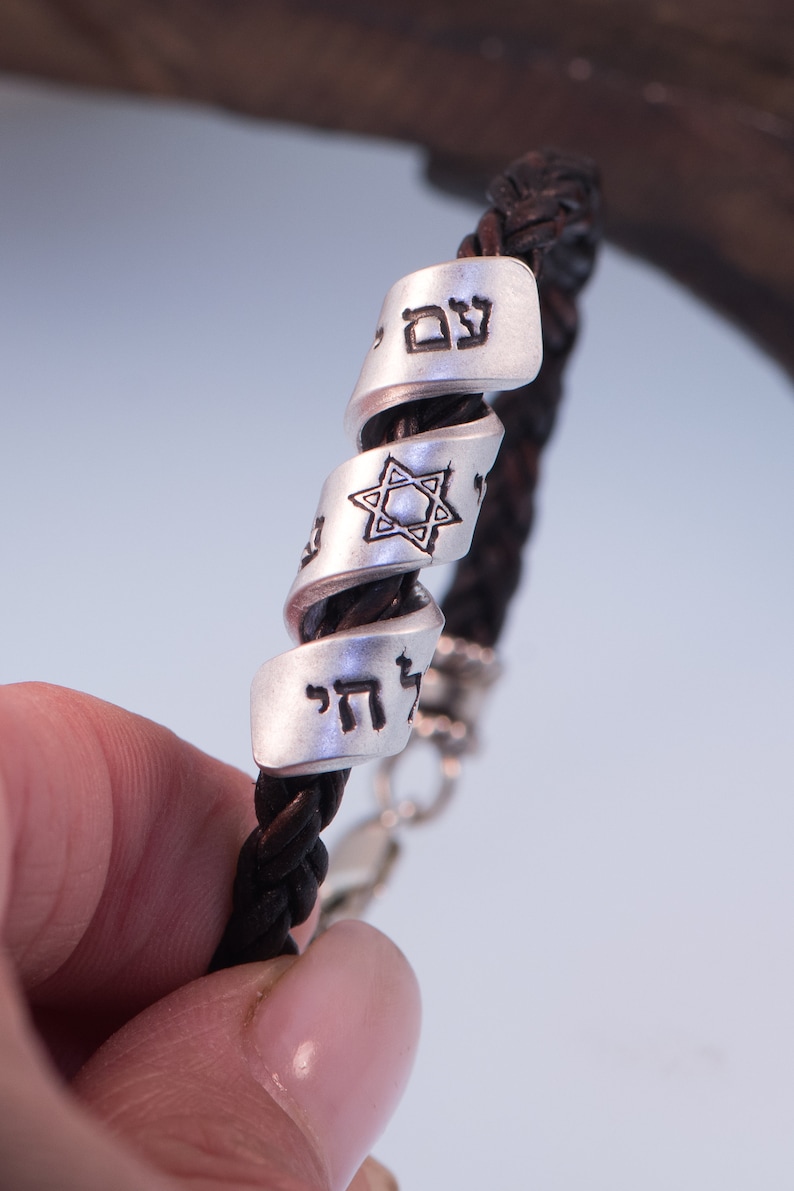 May include: A brown leather bracelet with silver charms featuring Hebrew text and a Star of David.