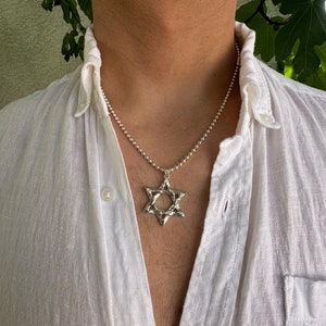 Puede incluir: Un collar de cadena de plata con un colgante de plata texturizado en forma de Estrella de David.