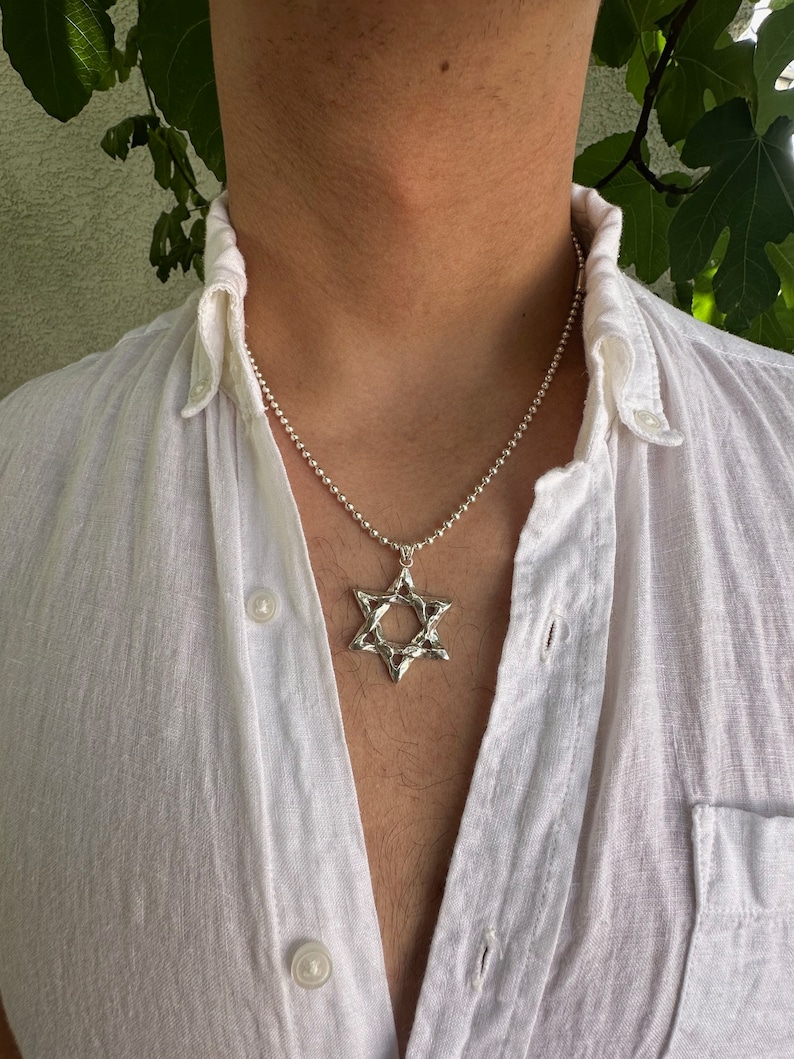Puede incluir: Un collar de cadena de plata con un colgante de plata texturizado en forma de Estrella de David.