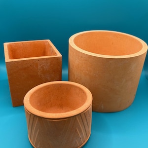 May include: Three terracotta colored concrete planters, one square, one round, and one round with a geometric pattern.
