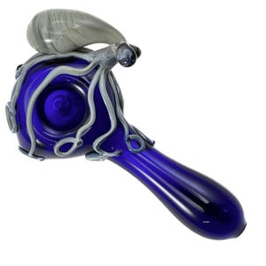 May include: A handcrafted glass pipe in a deep blue hue, featuring an octopus design. The octopus has gray tentacles and a bulbous head, adding a unique artistic touch. The pipe's bowl and stem are seamlessly integrated, creating a smooth, elegant form.