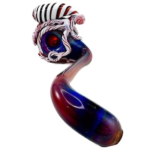 May include: A colorful glass pipe with a unique design. The pipe features a bulbous bowl with red, white, and blue accents, and a long, curved stem. The bowl has a red center, and the stem transitions from red to blue. The pipe is approximately 8 inches long.