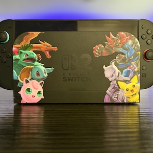 May include: Black Nintendo Switch console with colorful character stickers. The stickers feature various characters from the Pokemon franchise. The console has attached controllers and the text "Nintendo Switch".
