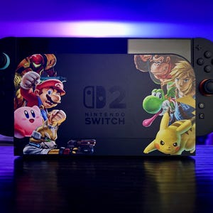 May include: A black Nintendo Switch console with a custom skin featuring characters like Mario, Kirby, and Pikachu. The console is on a dark surface, with a purple and blue gradient background. The Nintendo Switch logo is visible.