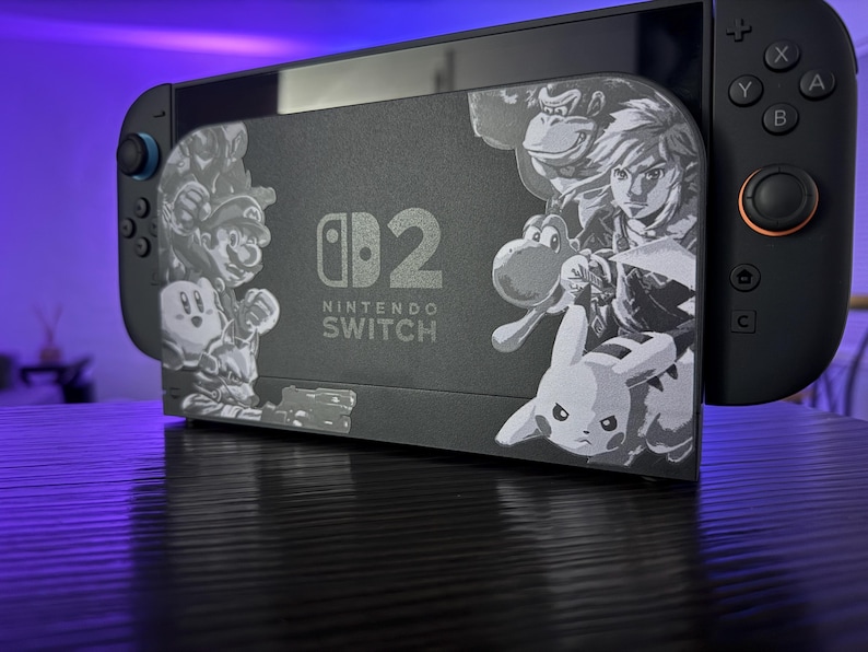 May include: A black Nintendo Switch console with a custom dock featuring engraved images of Mario, Kirby, Donkey Kong, Link, Yoshi, and Pikachu. The dock has the Nintendo Switch logo and the number 2.