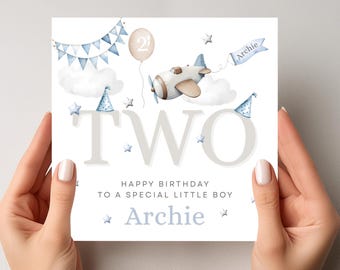 May include: A birthday card with a watercolour design. The card features a light blue aeroplane, a balloon with the number 2, and the word "TWO" in large letters. The text reads "Happy Birthday to a special little boy Archie."