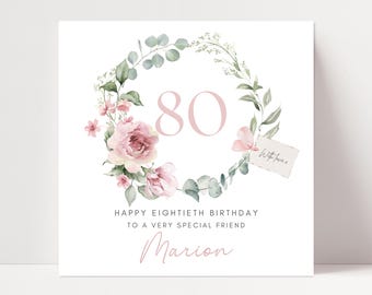 May include: A white greeting card with a floral wreath design. The card features the number 80 in pink, surrounded by pink flowers and green leaves. Text reads "Happy Eightieth Birthday to a Very Special Friend" and "Marion."