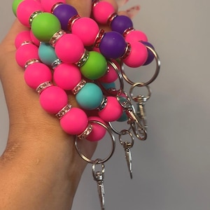 May include: A colorful beaded keychain with pink, green, blue, and purple beads. The keychain has a silver key ring and a silver charm.