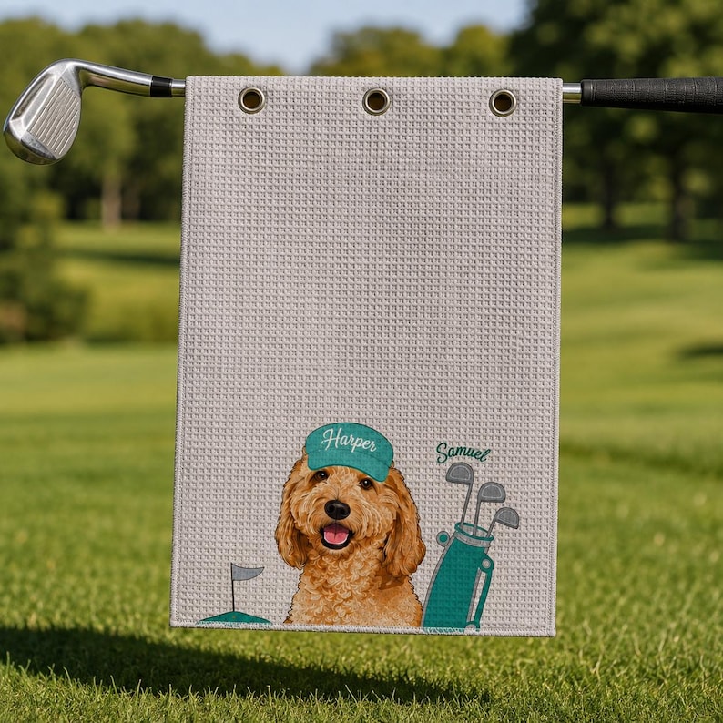 Puede incluir: Una toalla de golf de color gris claro con textura de gofre que presenta un golden doodle bordado con una gorra verde con el nombre Harper, una bolsa de golf verde con el nombre Samuel y una peque&ntilde;a bandera, colgada de un palo de golf.