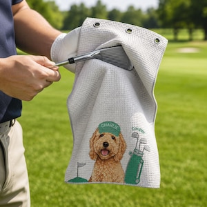 Puede incluir: Una toalla de golf de color gris claro con textura de gofre que presenta un golden doodle bordado con una gorra verde con el nombre Charlie, una bolsa de golf verde con el nombre Cooper y una bandera de golf. Tiene tres ojales met&aacute;licos.
