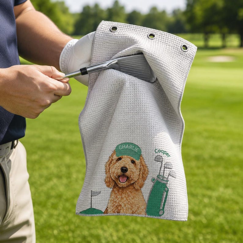 Puede incluir: Una toalla de golf de color gris claro con textura de gofre que presenta un golden doodle bordado con una gorra verde con el nombre Charlie, una bolsa de golf verde con el nombre Cooper y una bandera de golf. Tiene tres ojales met&aacute;licos.
