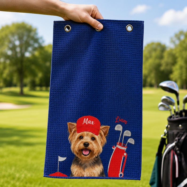 Puede incluir: Una toalla de golf rectangular de color azul marino con textura de gofre, que presenta un gr&aacute;fico de un Yorkshire Terrier con una gorra roja con el nombre Max, una bolsa de golf roja con palos y el nombre Liam bordado en rojo.