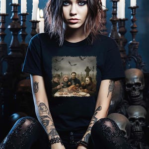 May include: Black t-shirt featuring a Halloween-themed graphic of horror movie characters gathered around a table. The image includes a graveyard scene with bats and a turkey dinner. The shirt is a crew neck.
