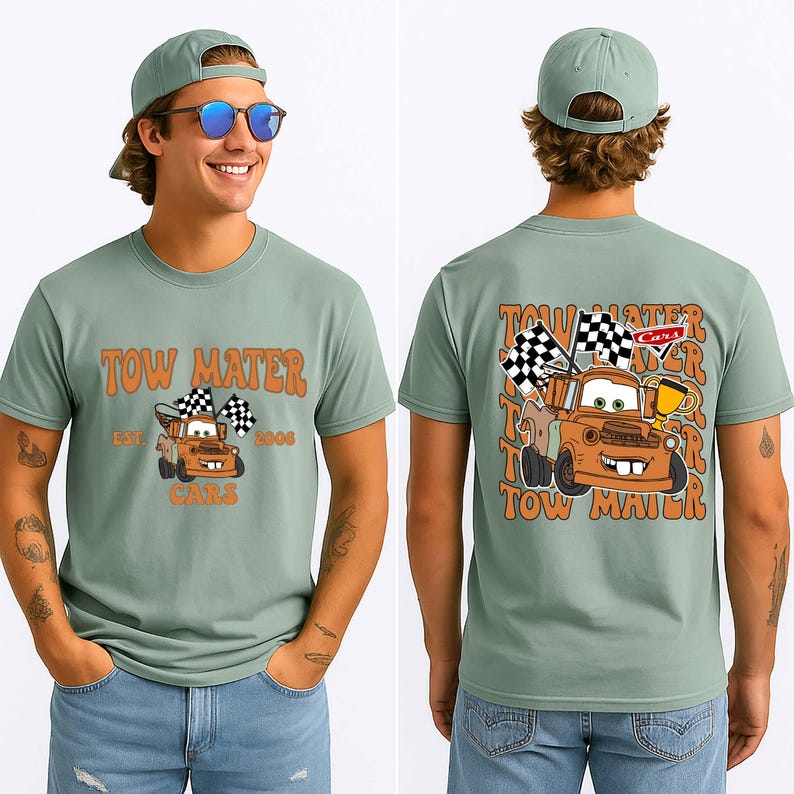 May include: Sage green t-shirt with a cartoon image of Tow Mater from the Cars film. The front of the shirt has the text "Tow Mater" and "Cars" with the year "2006". The back of the shirt has a larger image of Tow Mater with checkered flags.