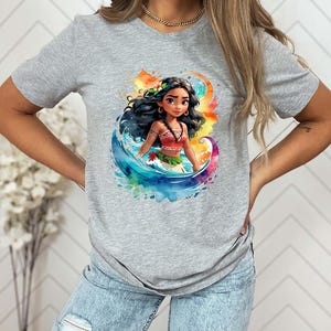 Peut inclure: T-shirt gris avec une illustration aquarelle color&eacute;e d'une princesse polyn&eacute;sienne aux longs cheveux noirs, v&ecirc;tue d'une tenue rouge et verte, debout dans les vagues de l'oc&eacute;an.
