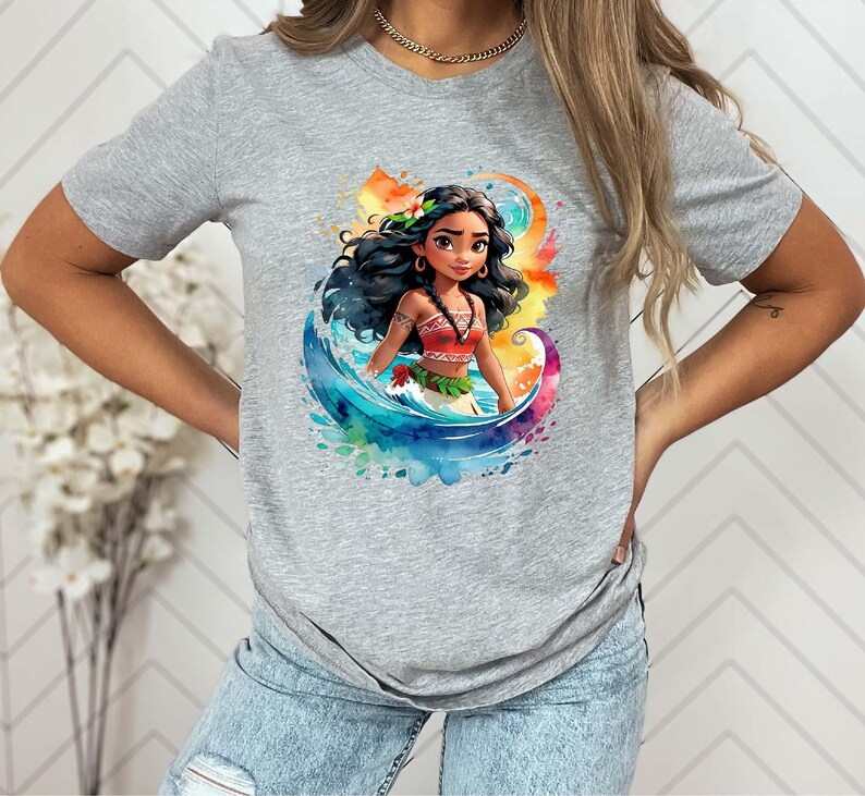 Peut inclure: T-shirt gris avec une illustration aquarelle color&eacute;e d'une princesse polyn&eacute;sienne aux longs cheveux noirs, v&ecirc;tue d'une tenue rouge et verte, debout dans les vagues de l'oc&eacute;an.