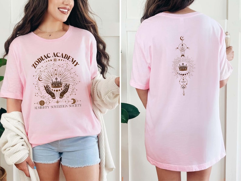 May include: Pink t-shirt with a brown graphic design featuring a crown, hands, and the text "Zodiac Academy Almighty Sovereign Society".