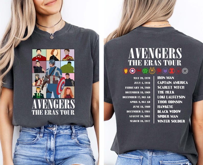 May include: A dark grey t-shirt with a graphic of the Avengers characters in a grid pattern. The text "Avengers The Eras Tour" is printed below the graphic. The back of the shirt has the text "Avengers The Eras Tour" printed at the top and a list of the Avengers characters with their corresponding dates.