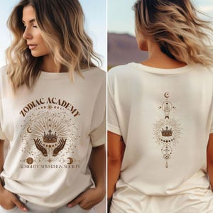 May include: A white t-shirt with a brown graphic design that says "Zodiac Academy Almighty Sovereign Society" with a crown and celestial symbols.