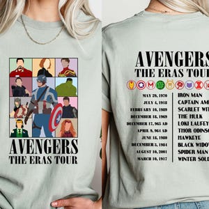 May include: A light green t-shirt with a graphic of the Avengers characters. The text "Avengers The Eras Tour" is printed on the shirt. The back of the shirt lists the Avengers characters and their first appearances.