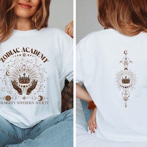 May include: White t-shirt with a brown graphic design featuring a crown, stars, and the text "Zodiac Academy Almighty Sovereign Society". The back of the shirt has a similar design with a crown, stars, and moons.