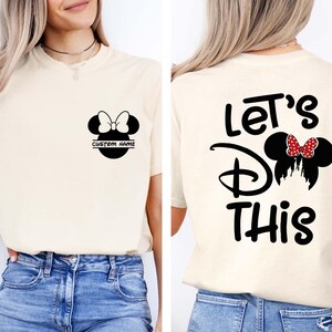 May include: Cream-colored t-shirt featuring a black Minnie Mouse design with a bow and the text "CUSTOM NAME" on the front. The back of the shirt displays the words "Let's Do This" with a Minnie Mouse silhouette.