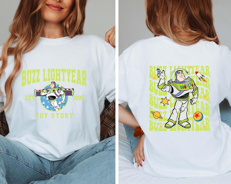 K&ouml;nnte beinhalten: Wei&szlig;es T-Shirt mit einem gr&uuml;nen und blauen Motiv von Buzz Lightyear aus Toy Story. Der Text "Buzz Lightyear" befindet sich in einem gelben Bogen &uuml;ber dem Motiv. Der Text "Est. 1995" befindet sich unter dem Motiv. Der Text "Toy Story" befindet sich unter dem Text "Est. 1995".