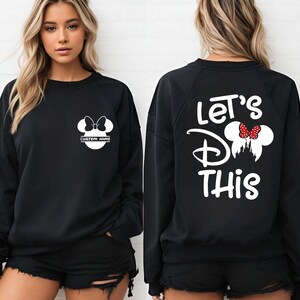 May include: Black sweatshirt with white Minnie Mouse graphic on the front and back. The front graphic includes a bow and space for a custom name. The back features the text "Let's Do This" with a Minnie Mouse design.
